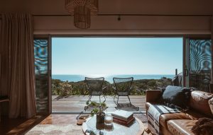 Interior design of luxurious apartment with large balcony doors and wooden terrace having picturesque view on green forested seashore and calm blue sea